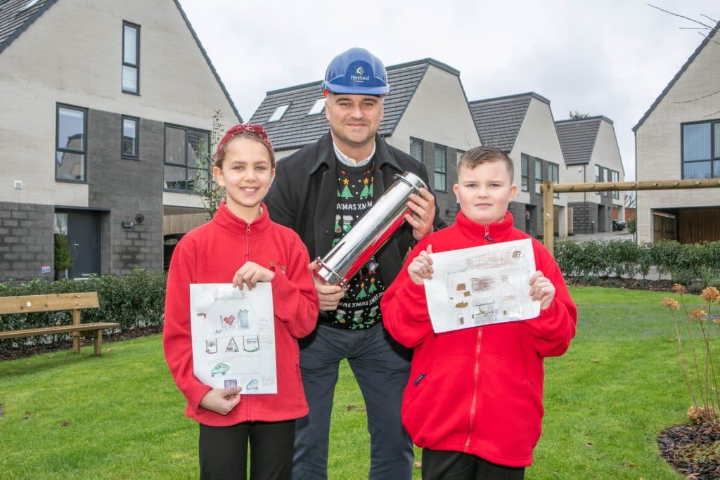 Paul Kitchingman Managing Director of Pentland Homes holding a time capsule with two school children.