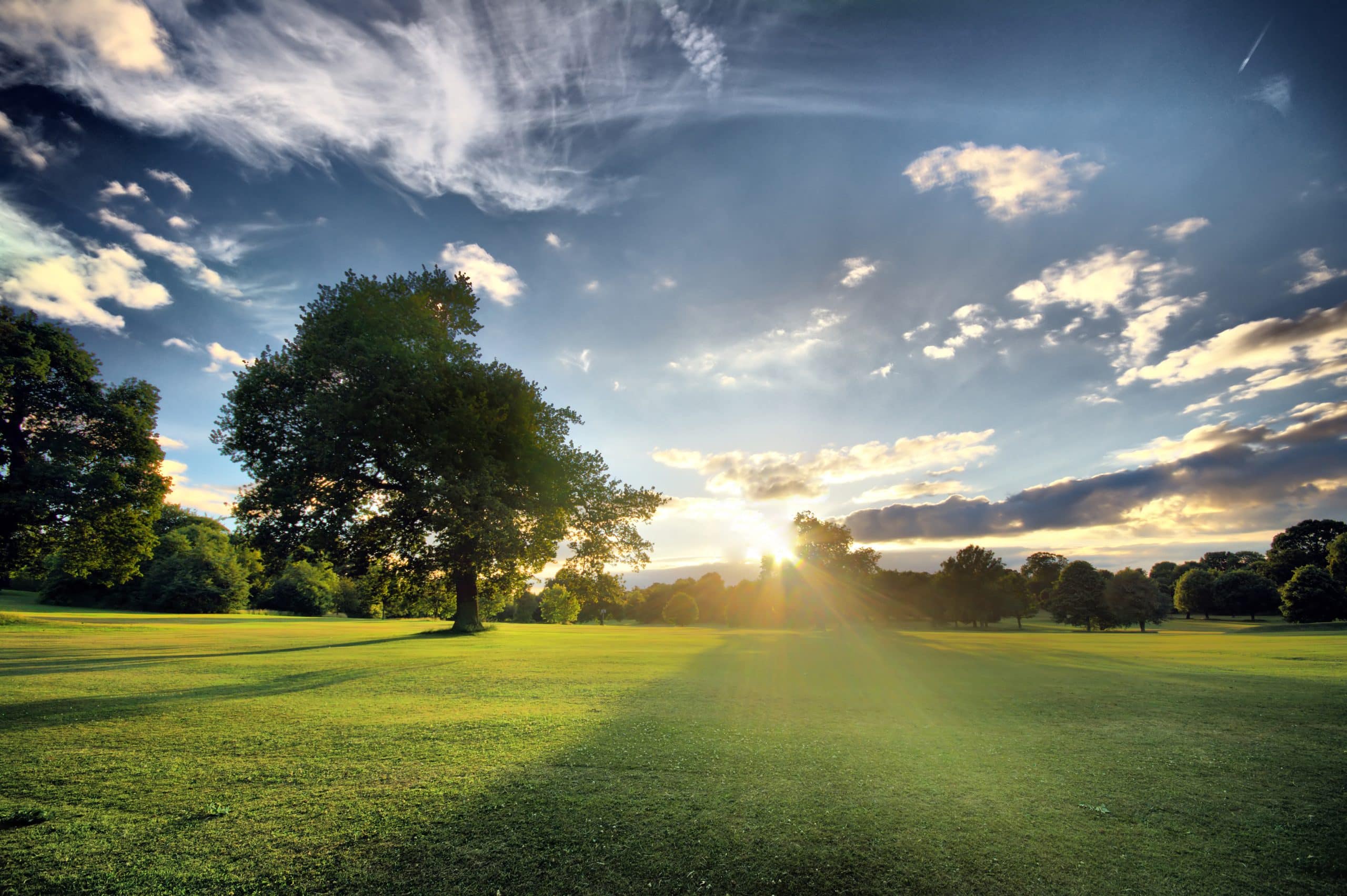 A sunset over a golf course, with the sun breaking through the clouds.