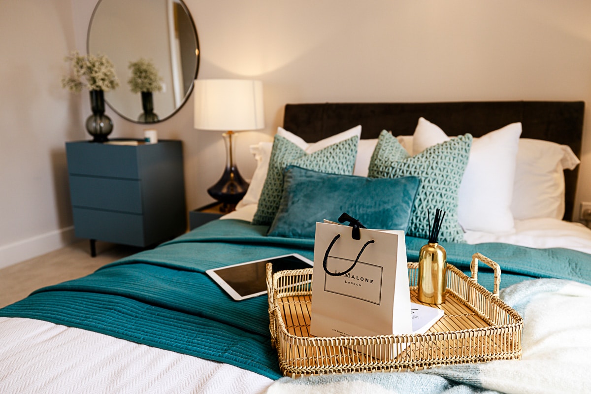 A bedroom at Terlingham Gardens, showing a bed with a tablet on it and a Jo Malone bag.