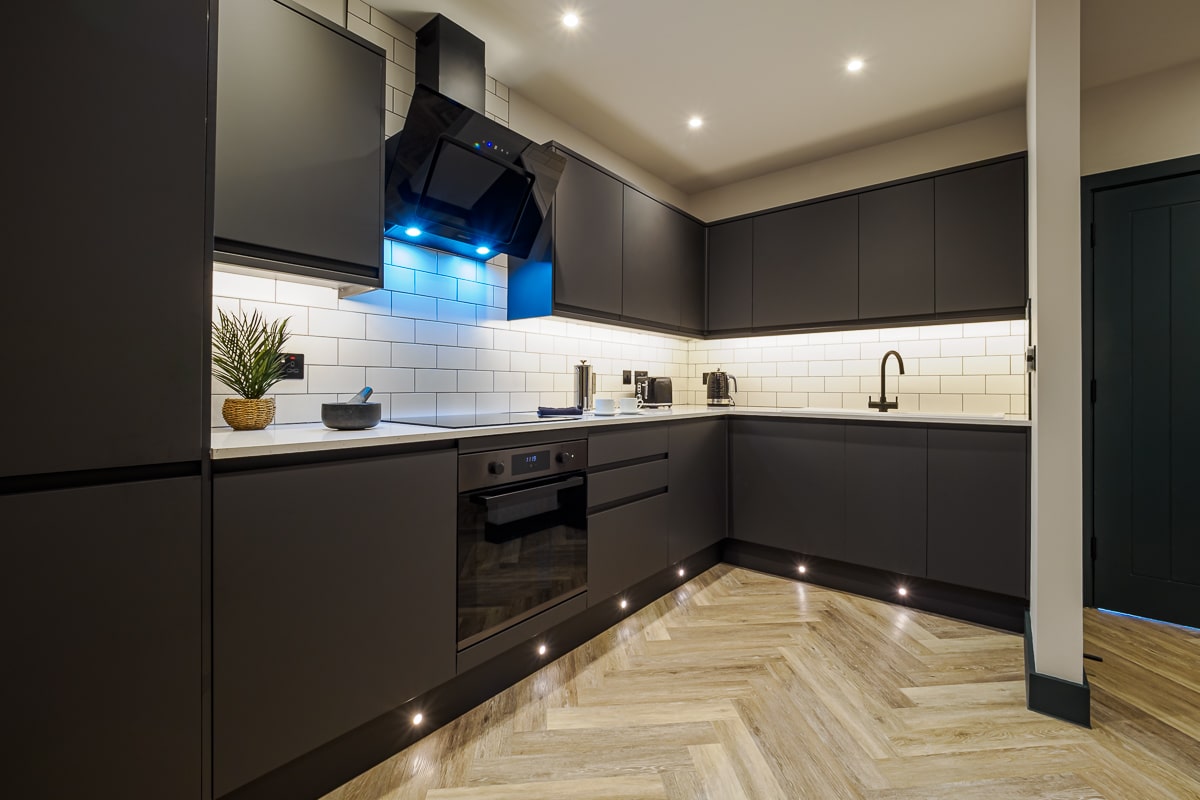 A kitchen in a Hawker6 apartment showing herringbone floor and black cupboards.