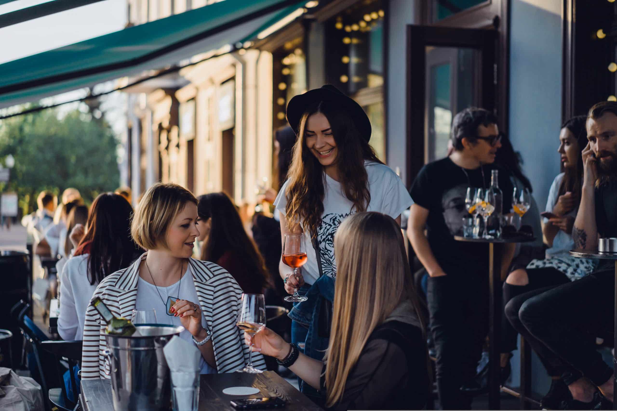 A waitress serving two people at a restaurant. She is passing them a glass of wine, smiling.