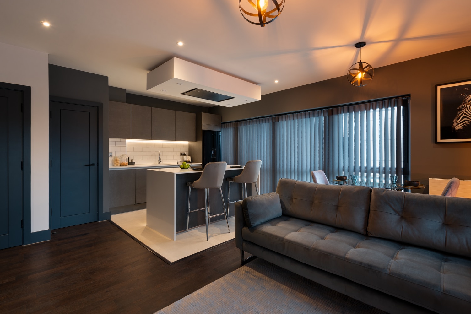 The open plan kitchen/diner and living area of a Hawker6 apartment home. With a sofa, kitchen island and large windows.