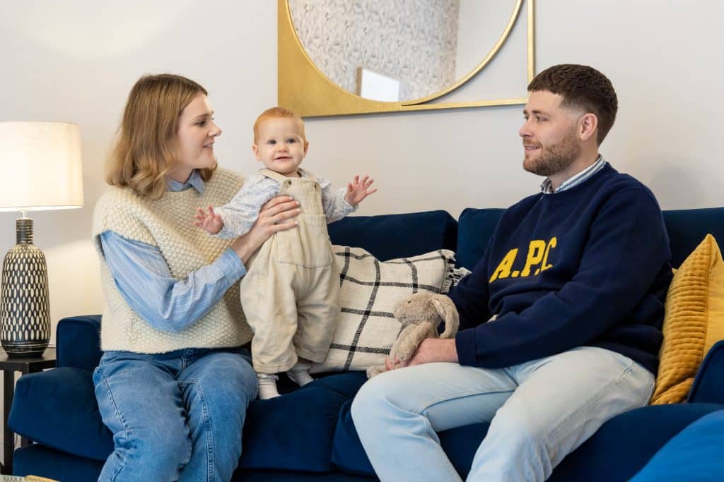 Pentland Homes customers sat on a sofa with their baby smiling.