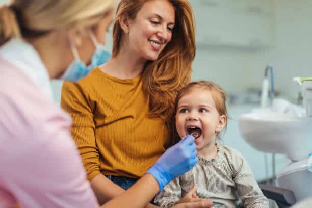 Young girl having her dental check up done next to her mum by a dentist.